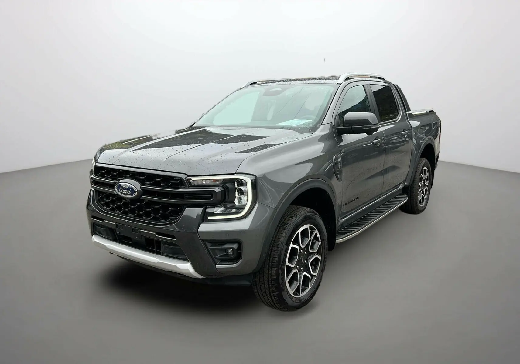 Ford Ranger 2025 gris carbone en 3/4 avant droit, avec jantes alliage et calandre noire distinctive Wildtrak Plus.
