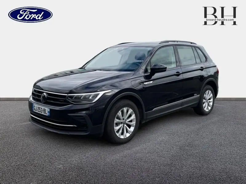 Volkswagen Tiguan 1.4 eHybrid noir nacré en 3/4 avant droit, avec jantes alu et barres de toit visibles.