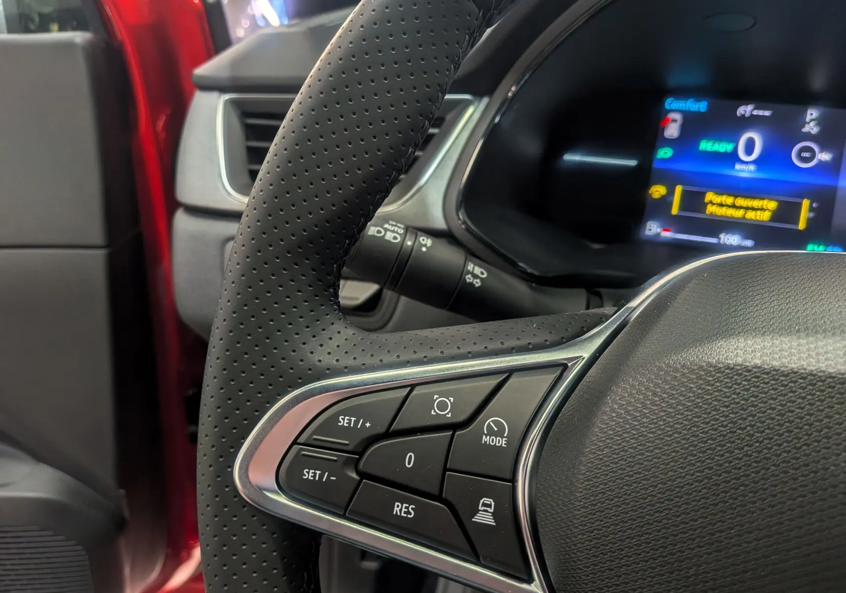 Gros plan sur le volant perforé du Renault Captur E-TECH 2025 rouge Flamme, avec affichage numérique du tableau de bord en arrière-plan.