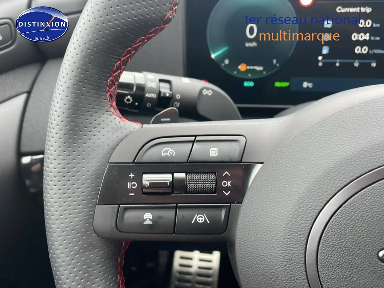 Gros plan sur le volant sport en cuir noir avec surpiqûres rouges du Hyundai Tucson gris écotronique, affichage digital en arrière-plan.