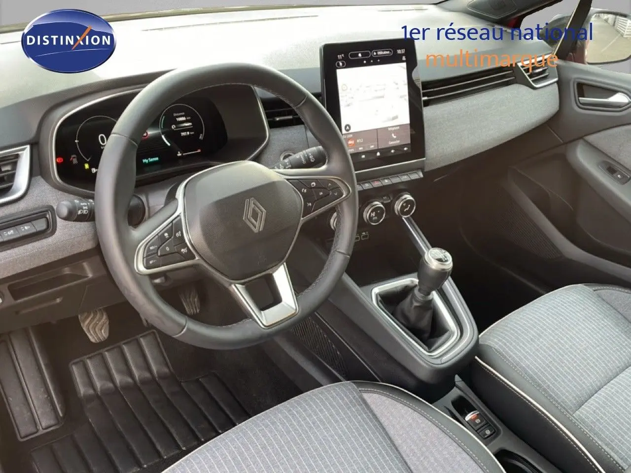 Vue intérieure de face du poste de conduite de la Renault Clio 2025 avec volant cuir, écran tactile vertical et boîte manuelle.