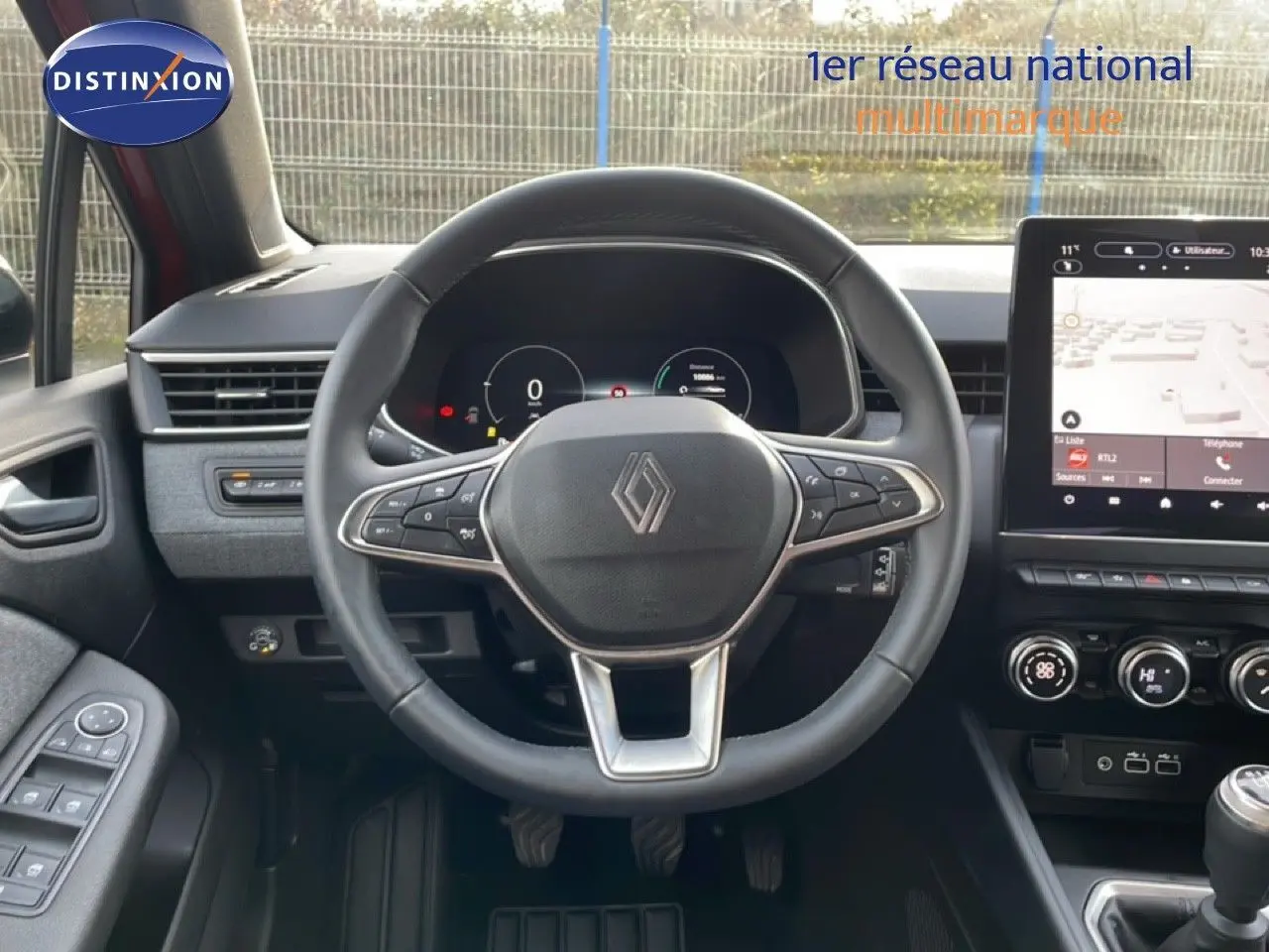 Vue intérieure centrée sur le volant cuir de la Renault Clio rouge Désir Métal 2025 avec tableau de bord numérique et écran tactile.