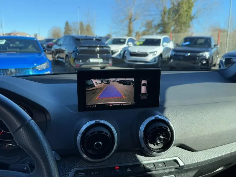 Vue intérieure du tableau de bord d’un Audi Q2 30 TDI S line 2024, écran de caméra de recul allumé, volant partiel visible.