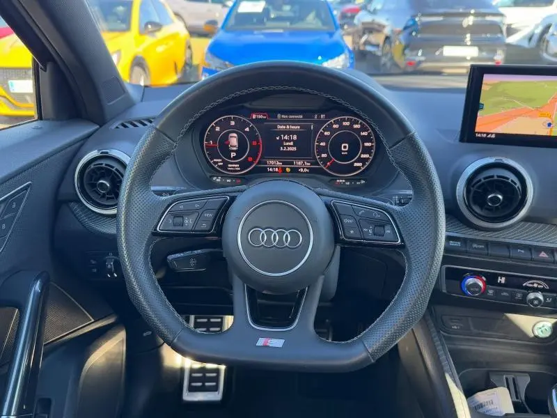 Vue intérieure centrée sur le volant sport Audi Q2 30 TDI S line, tableau de bord numérique et écran GPS visible.
