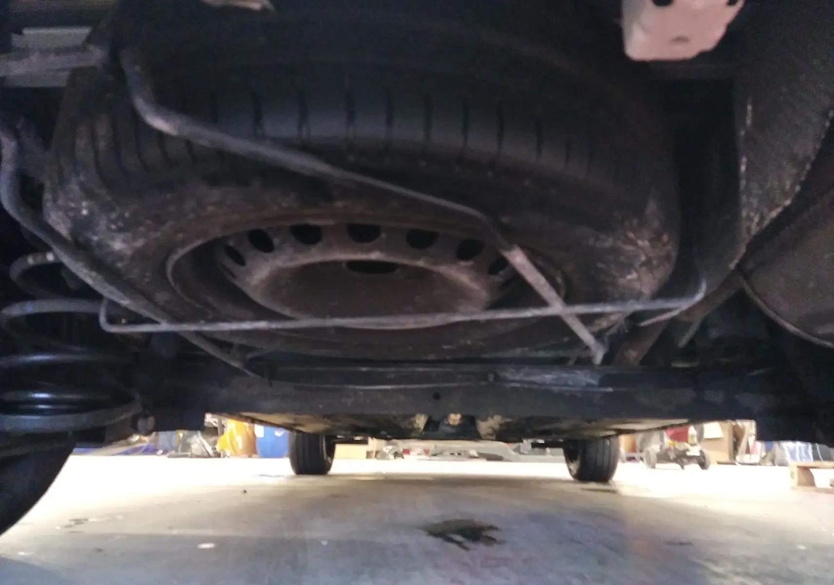 Vue sous le Renault Kangoo blanc 2019 montrant la roue de secours fixée sous le châssis et la suspension arrière.