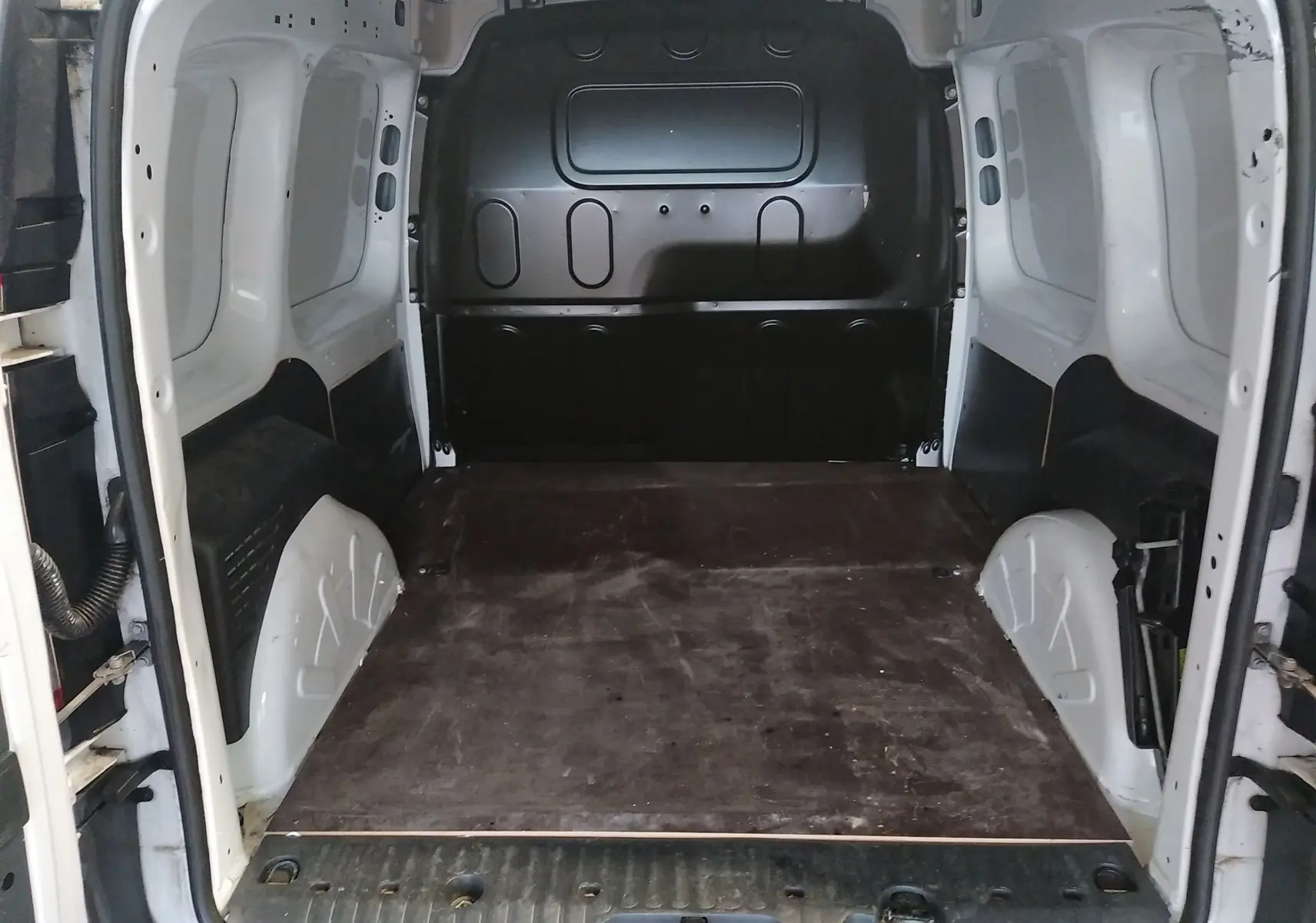 Vue arrière du Renault Kangoo blanc 2019 montrant l'espace de chargement vide avec plancher en bois et parois métalliques.