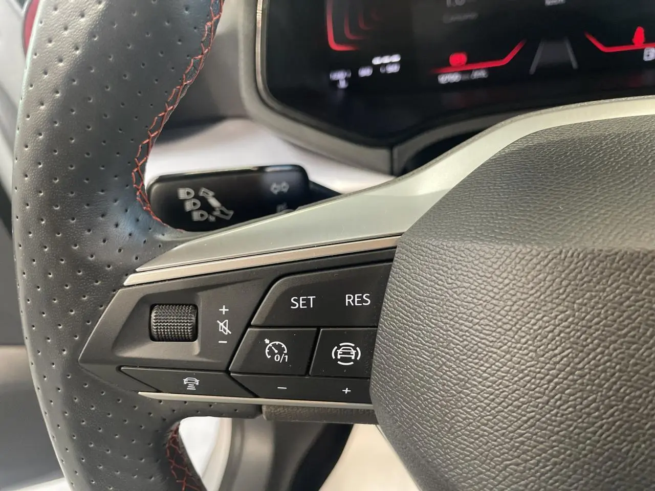 Gros plan sur les commandes du volant sport cuir noir perforé avec surpiqûres rouges du SEAT Arona 2024.