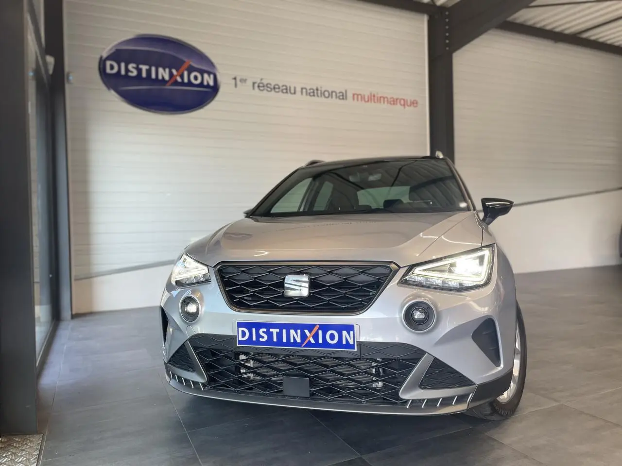 Vue de face d'un SEAT Arona 2024 gris GRS avec calandre noire et phares EcoLED allumés en showroom.