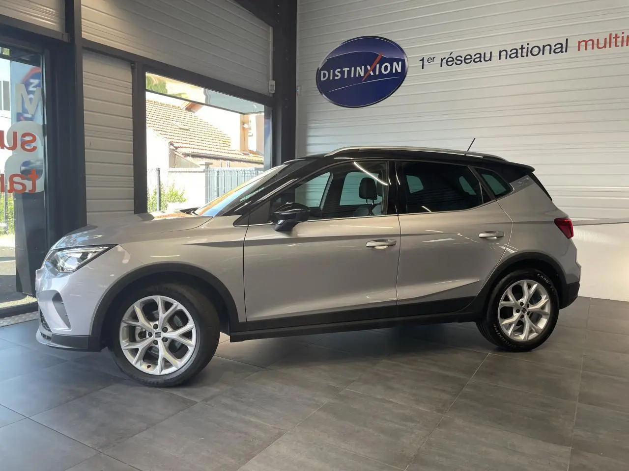 Vue latérale gauche d'un SEAT Arona 2024 gris GRS avec jantes alliage 16 pouces et toit noir en showroom.