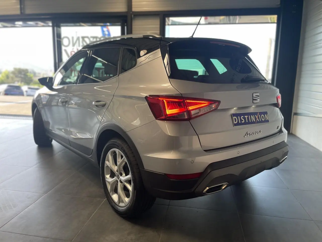 Vue 3/4 arrière droite d'un SEAT Arona 2024 rouge passion avec feux arrière allumés et jantes alliage 16 pouces.