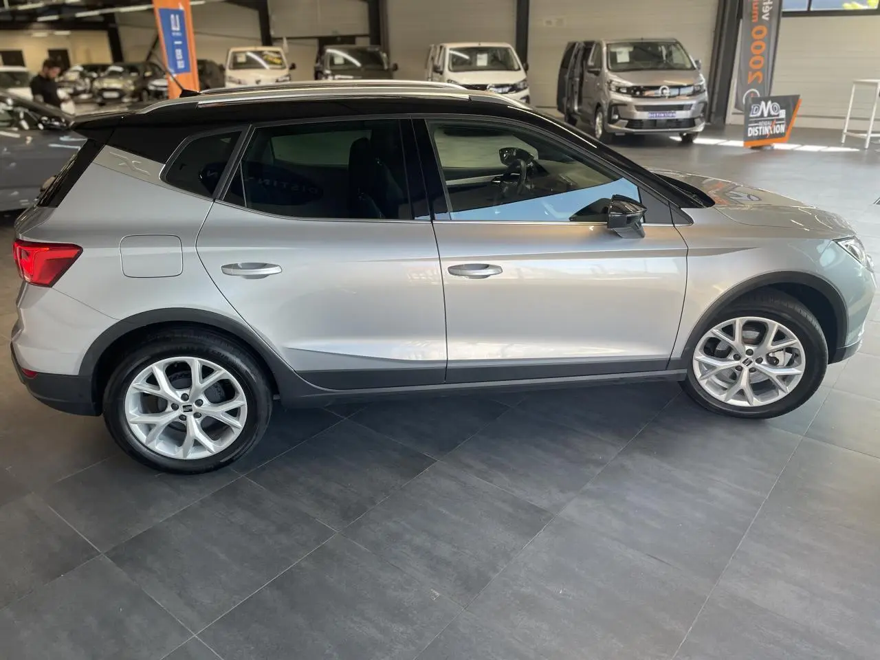 Vue latérale droite d'un SEAT Arona 2024 gris avec toit noir et jantes alliage 16 pouces en showroom.