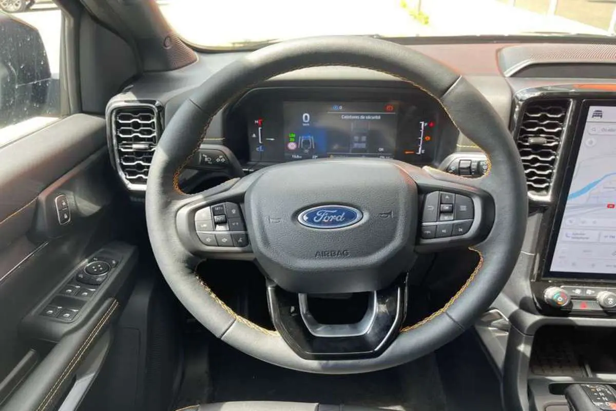 Vue intérieure centrée sur le volant du Ford Ranger 2025 noir agate, avec tableau de bord numérique et écran tactile visible.