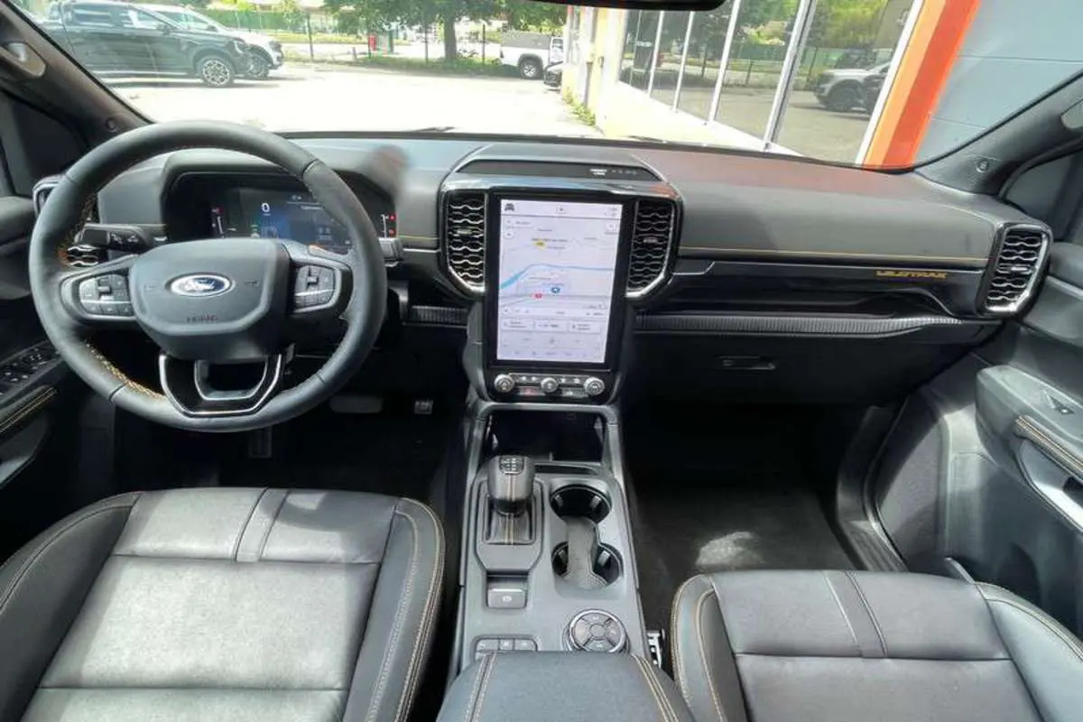 Vue intérieure du Ford Ranger 2025 Wildtrak Plus, tableau de bord noir avec écran tactile vertical et sellerie cuir noire.