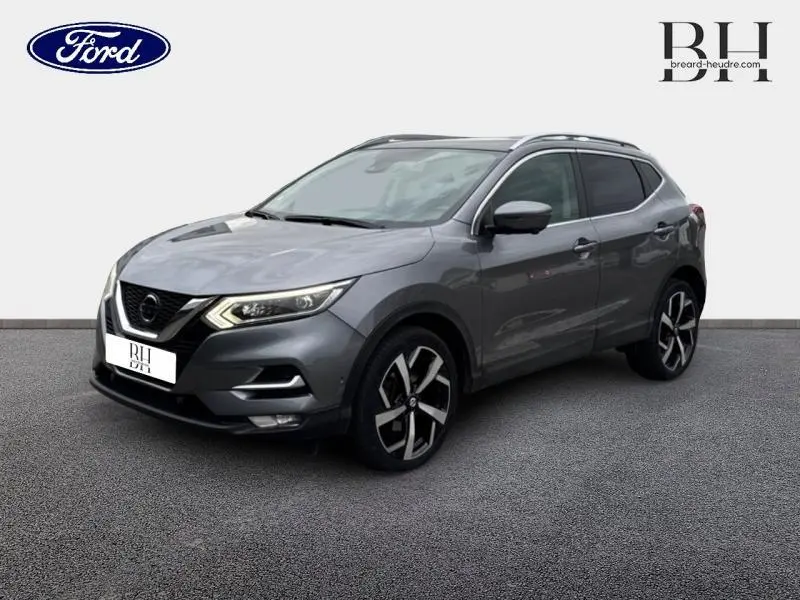 Nissan Qashqai gris Squale en 3/4 avant droit, avec jantes alliage noires et barres de toit visibles.