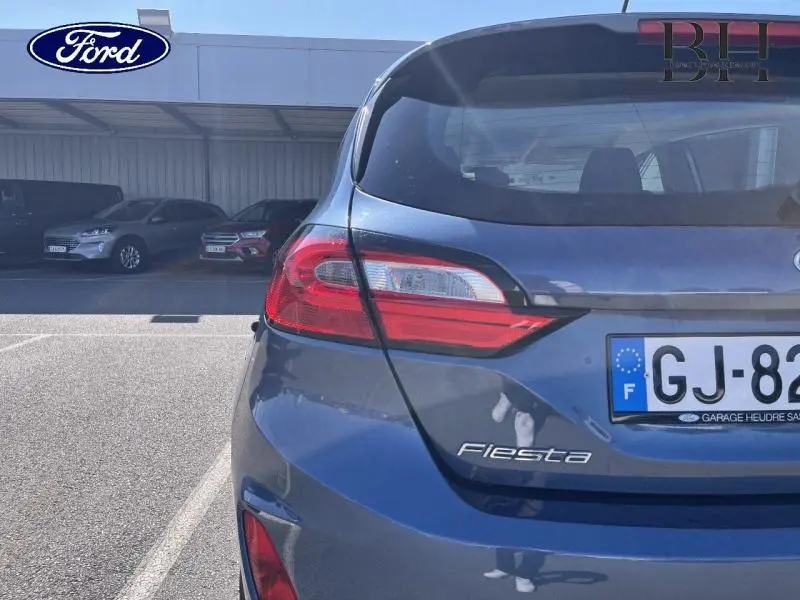 Vue arrière droite d'une Ford Fiesta 2022 bleu azur métallisé avec feux arrière LED et logo visible.