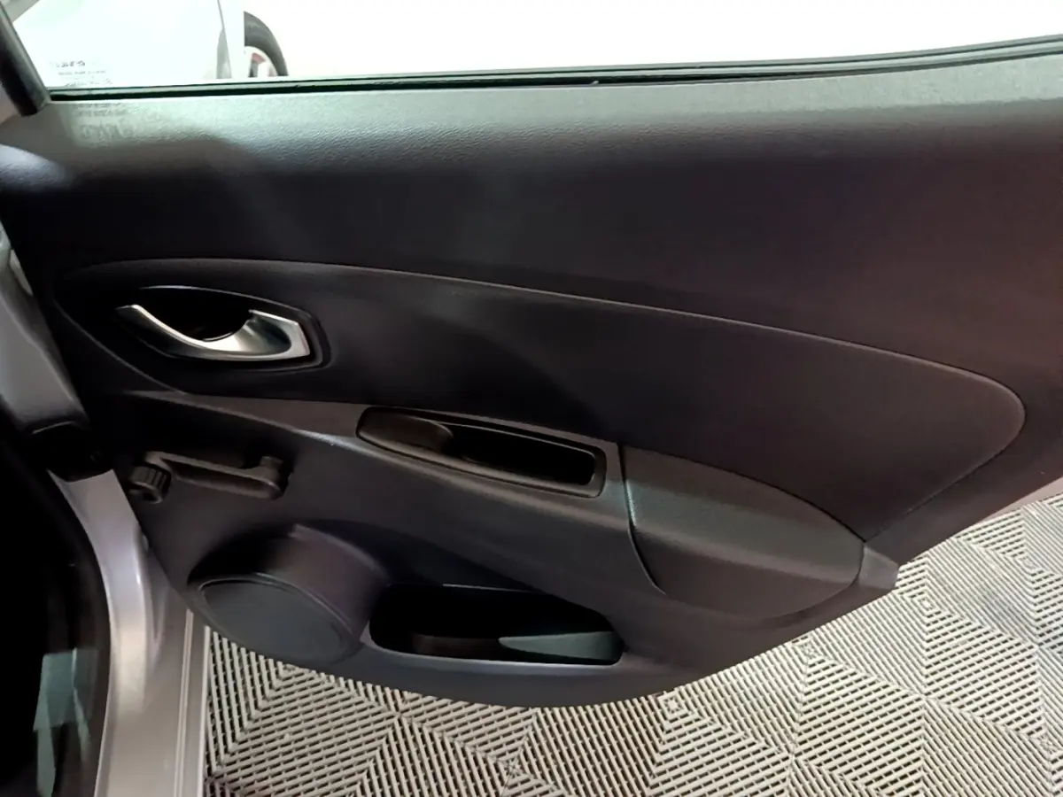 Vue intérieure côté gauche de la porte avant d’une Renault Clio gris clair, avec poignée argentée et commande manuelle de vitre.