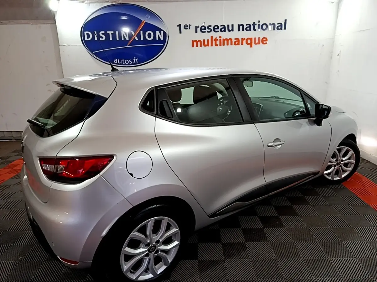 Vue 3/4 arrière droite d'une Renault Clio Business gris clair 2018 dans un showroom avec logo Distinxion en arrière-plan.