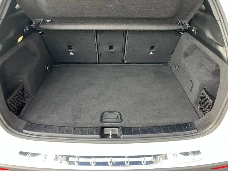 Coffre ouvert vu de l'arrière d'un Mercedes GLA 200 AMG Line blanc polaire avec intérieur noir et filets de rangement.