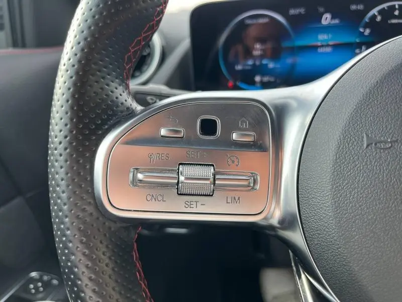 Gros plan sur les commandes argentées du volant sport en cuir perforé avec surpiqûres rouges du Mercedes GLA 200 AMG Line blanc polaire 2022.