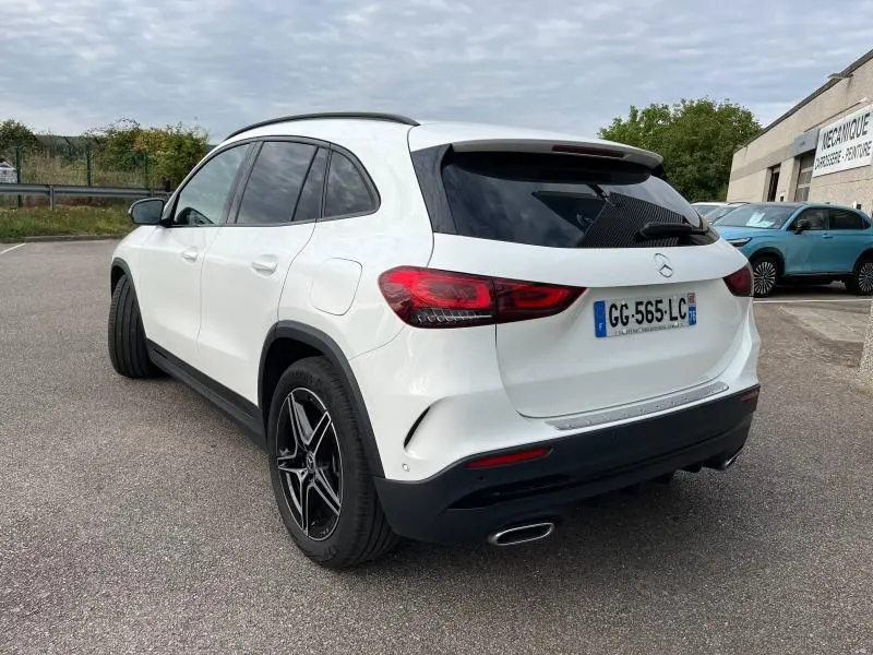 Vue 3/4 arrière droite d'un Mercedes GLA blanc polaire avec jantes AMG et vitres arrière teintées.
