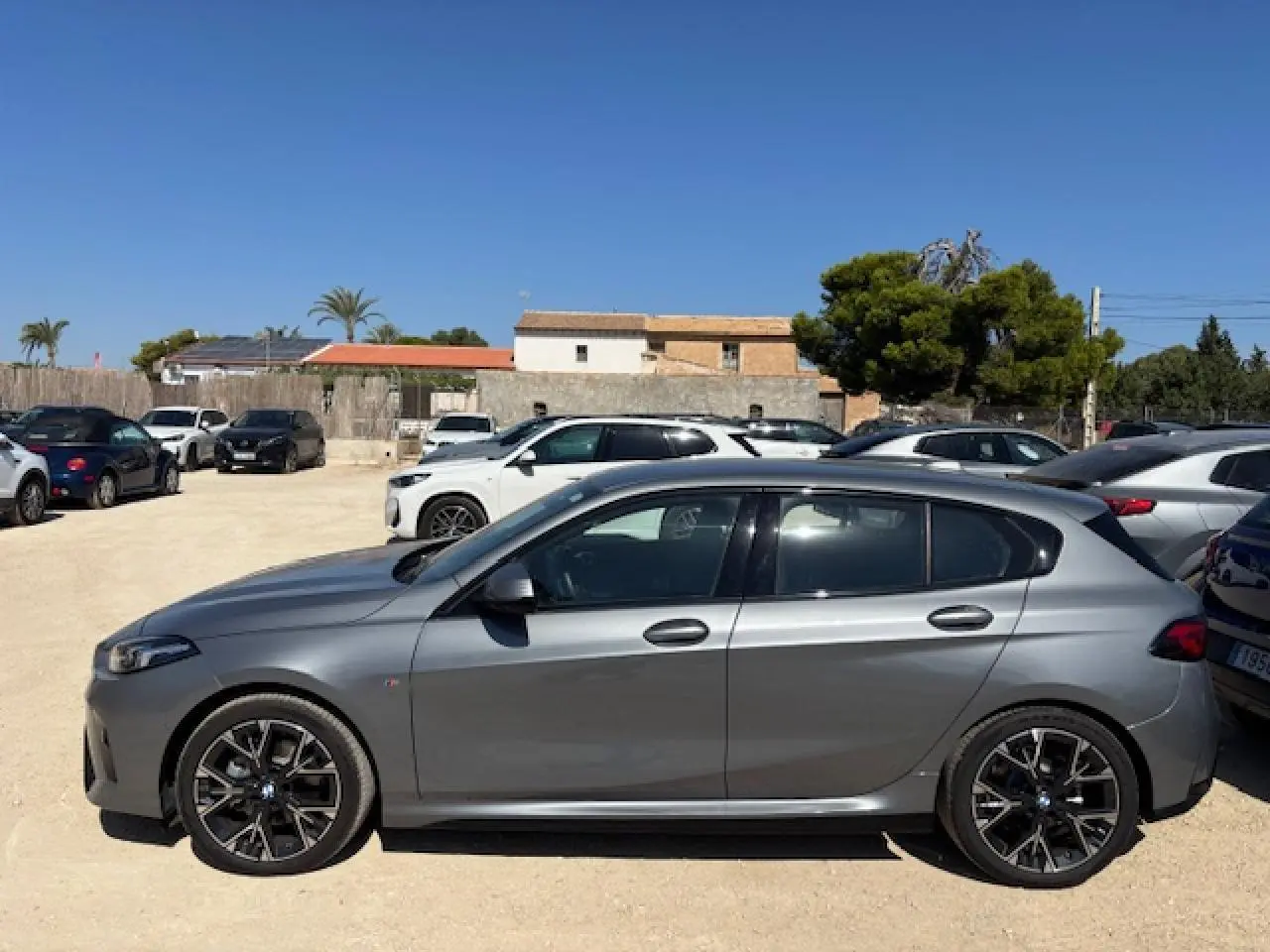 BMW Série 1 118d M Sport gris métallisé vue profil côté gauche sur parking ensoleillé