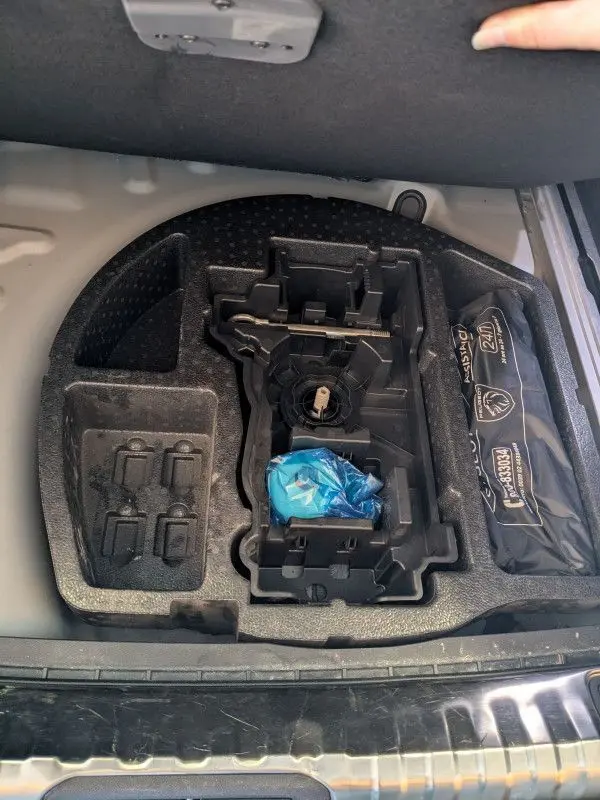 Compartiment de rangement sous le plancher du coffre du Peugeot 508 SW gris, avec trousse de secours et espace vide pour outils.