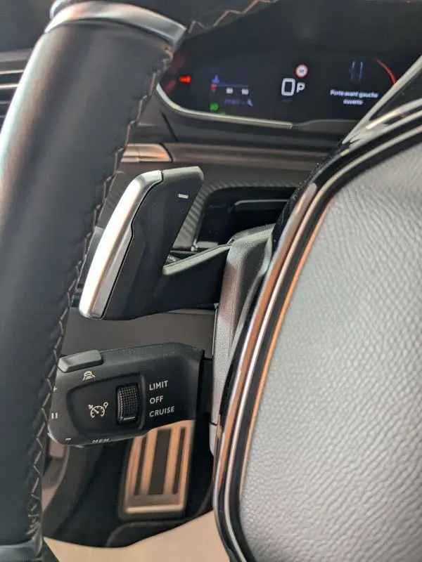Gros plan sur la commande de régulateur de vitesse et palettes au volant cuir noir du Peugeot 508 SW gris selenium 2024.