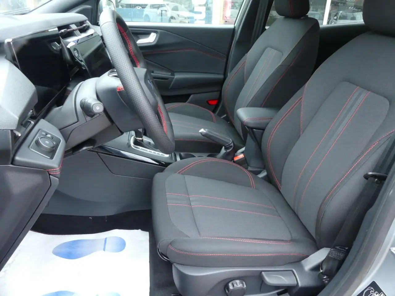 Vue intérieure côté gauche du Ford Puma 2025, sièges tissu gris avec surpiqûres rouges et volant sport.