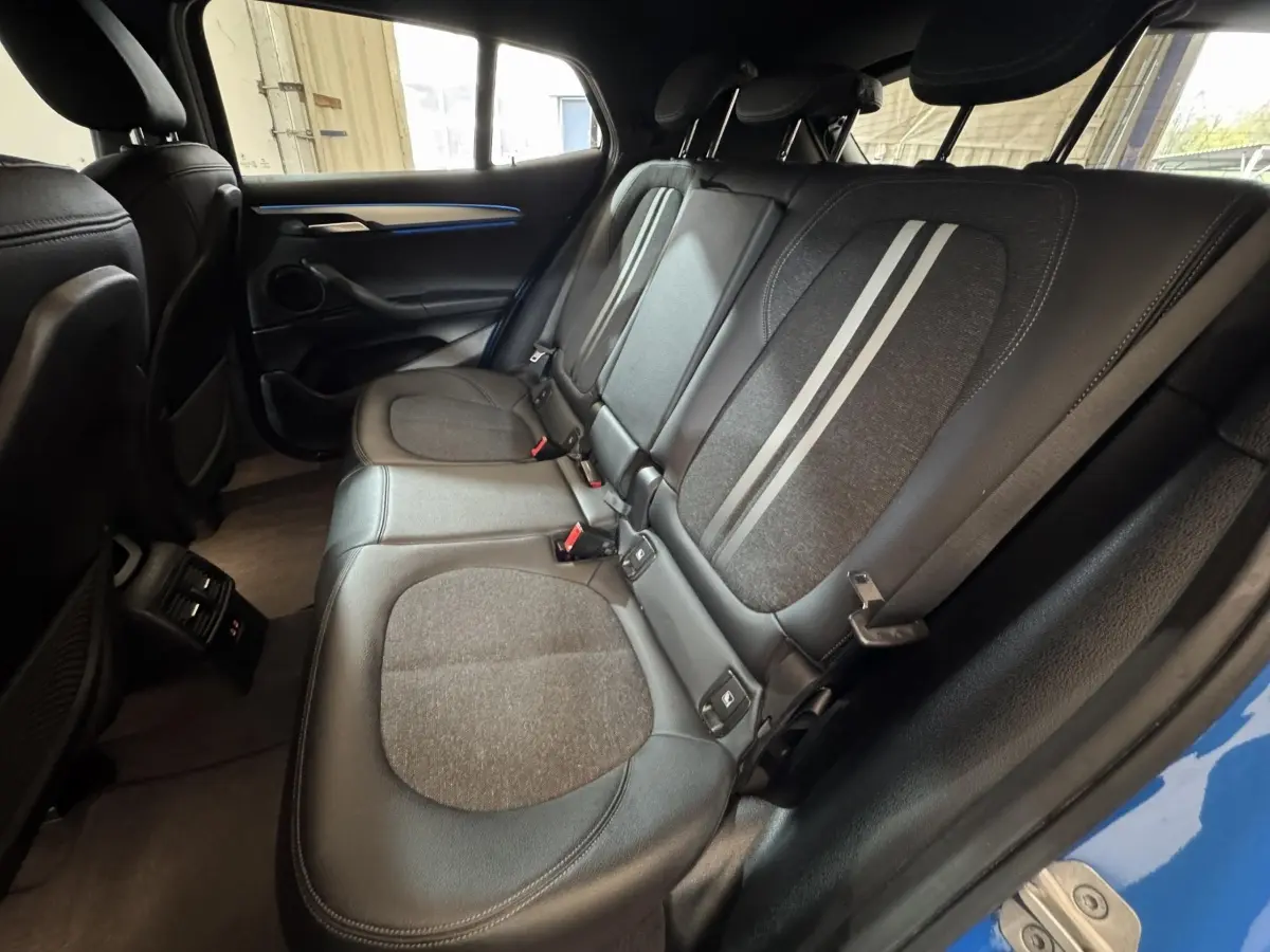 Vue intérieure arrière côté droit du BMW X2 xDrive25e bleu, montrant les sièges noirs avec bandes grises et ceinture de sécurité.