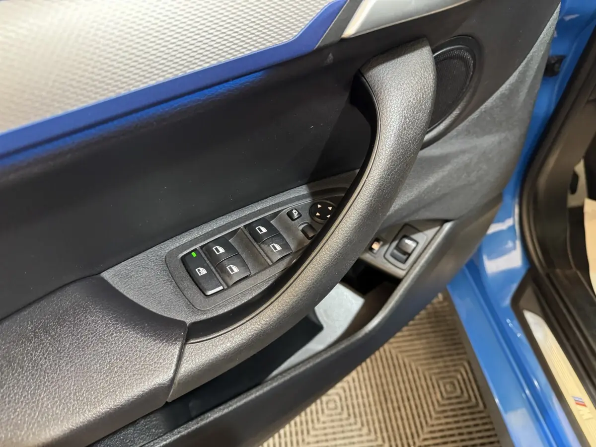 Gros plan sur la porte avant gauche bleu de la BMW X2 xDrive25e, avec commandes électriques des vitres et haut-parleur intégré.