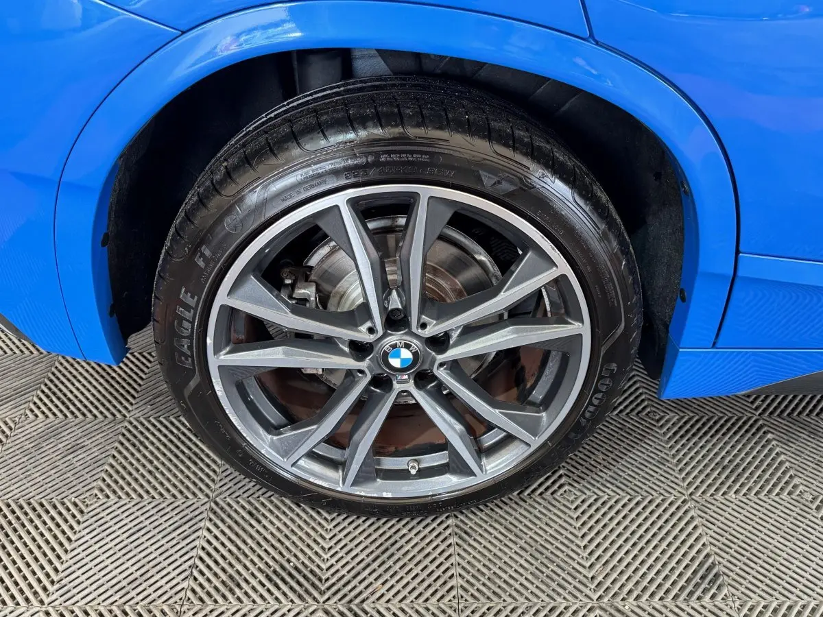 Gros plan sur la roue avant droite d’un BMW X2 bleu, avec jante alliage grise et logo BMW central.