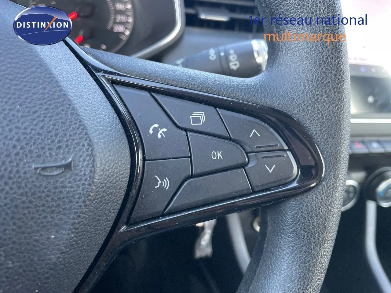 Gros plan sur les commandes au volant côté gauche d'une Renault Clio Société blanc glacier, tableau de bord en arrière-plan.