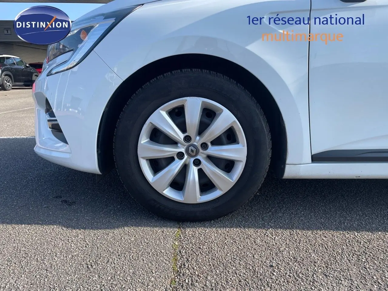 Gros plan sur la roue avant gauche d'une Renault Clio Société blanche Glacier, avec jante alliage et partie du pare-chocs visible.