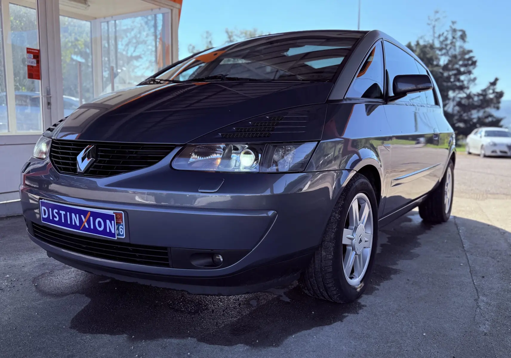 Renault Avantime gris en 3/4 avant droit, mettant en valeur sa silhouette unique et ses phares allumés.