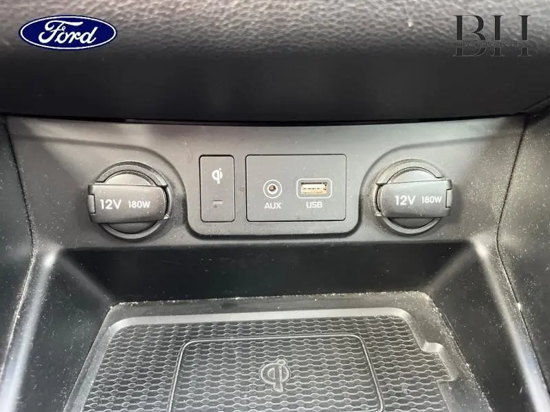 Vue rapprochée de la console centrale noire du Hyundai Tucson 2020 avec prises 12V, USB, AUX et chargeur sans fil Qi.