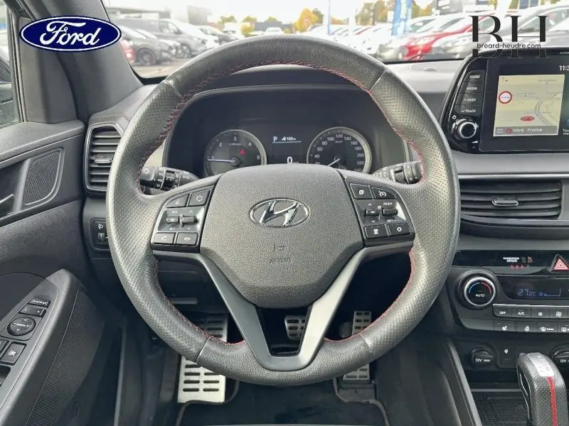 Vue centrée sur le volant cuir noir avec surpiqûres rouges du Hyundai Tucson Phantom Black Métal, tableau de bord et écran tactile visibles.