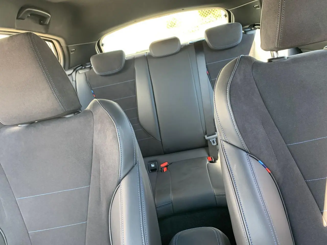 Intérieur arrière de la BMW Série 1 118d M Sport 2025 avec sièges Alcantara noirs et surpiqûres bleues visibles.