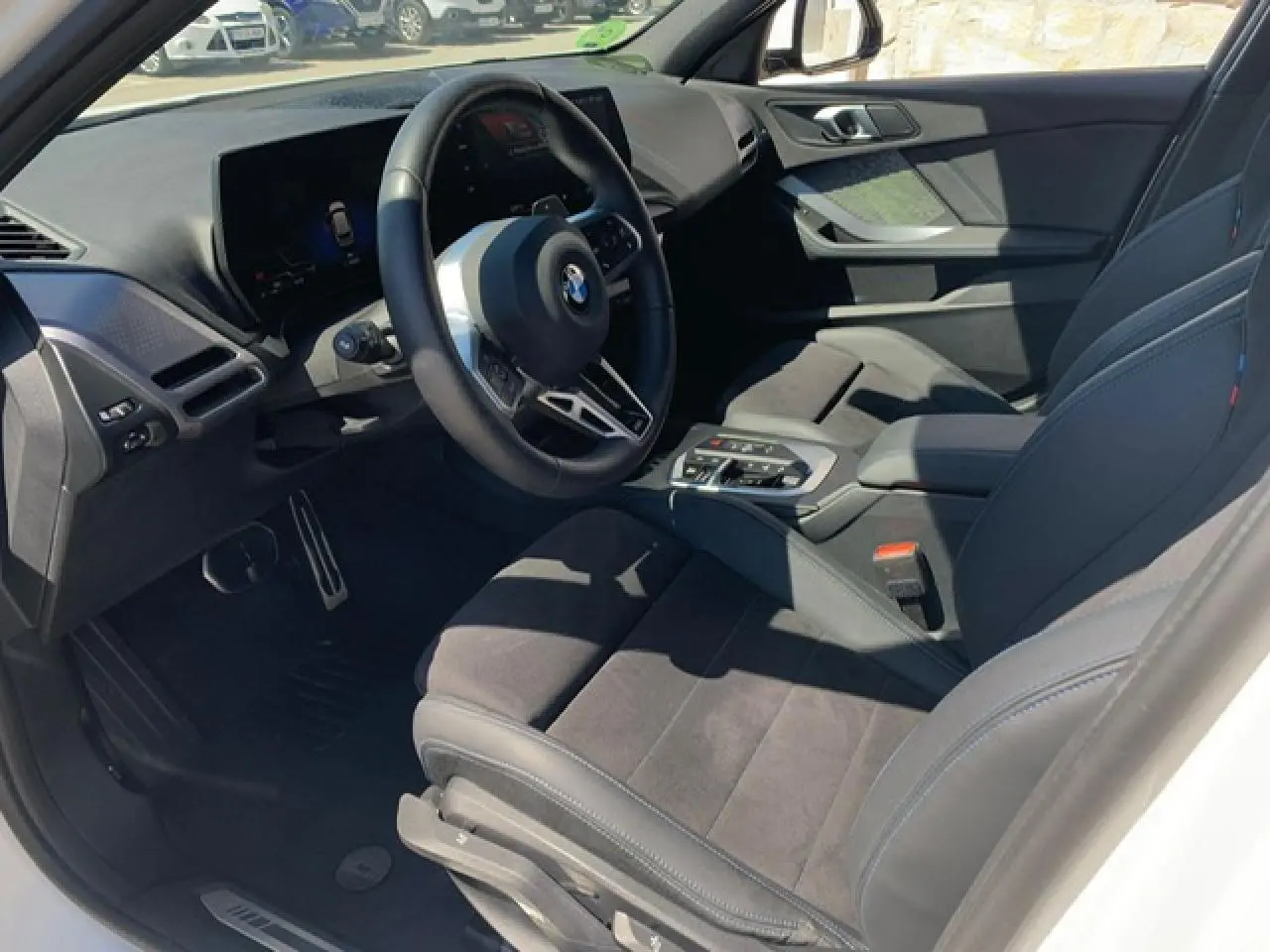 Intérieur côté conducteur de la BMW Série 1 118d 2025, sellerie Alcantara noire avec surpiqûres bleues et volant M cuir.