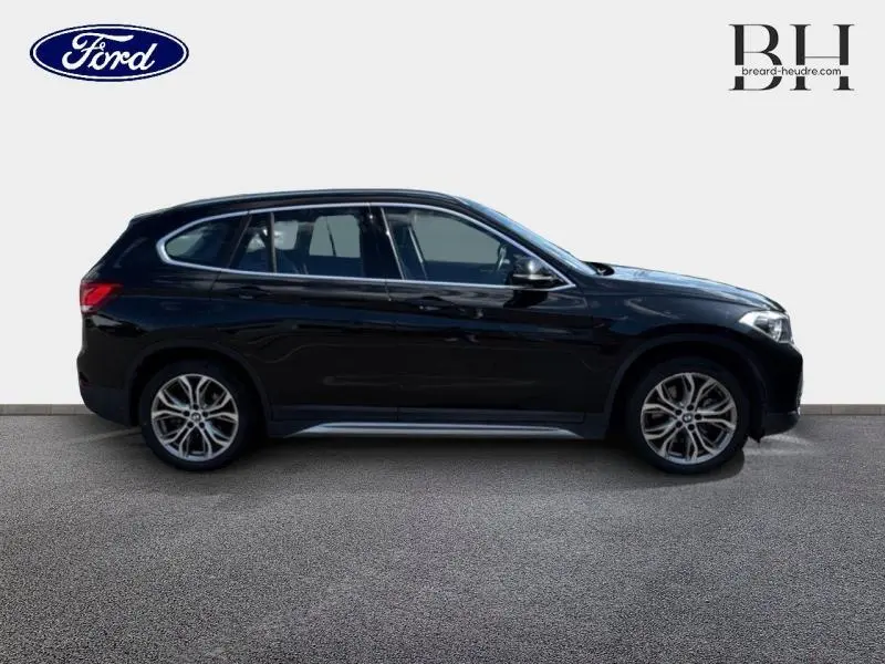 Profil côté gauche d'un BMW X1 xDrive25eA 220ch xLine 2021 en noir Saphirschwarz avec jantes alu et barres de toit.