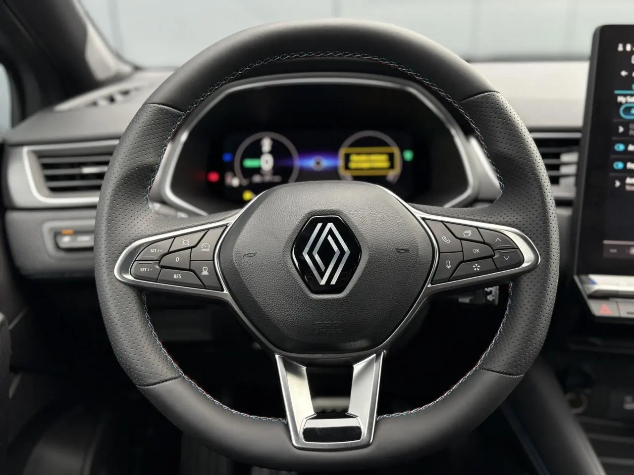 Vue frontale du volant noir avec surpiqûres tricolores du Renault Captur Esprit Alpine 2025, tableau de bord numérique en arrière-plan.