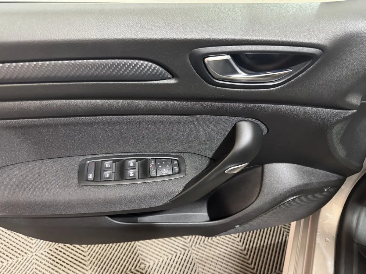 Gros plan sur la porte intérieure côté conducteur de la Renault Mégane gris clair, avec commandes des vitres et poignée noire.