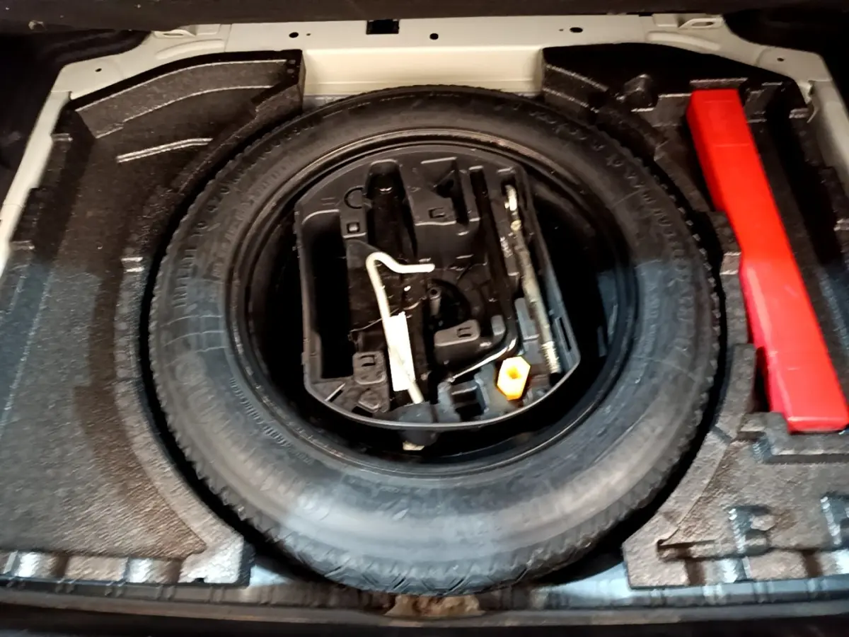 Vue rapprochée de la roue de secours et des outils dans le coffre d'une Peugeot 308 blanche de 2017.