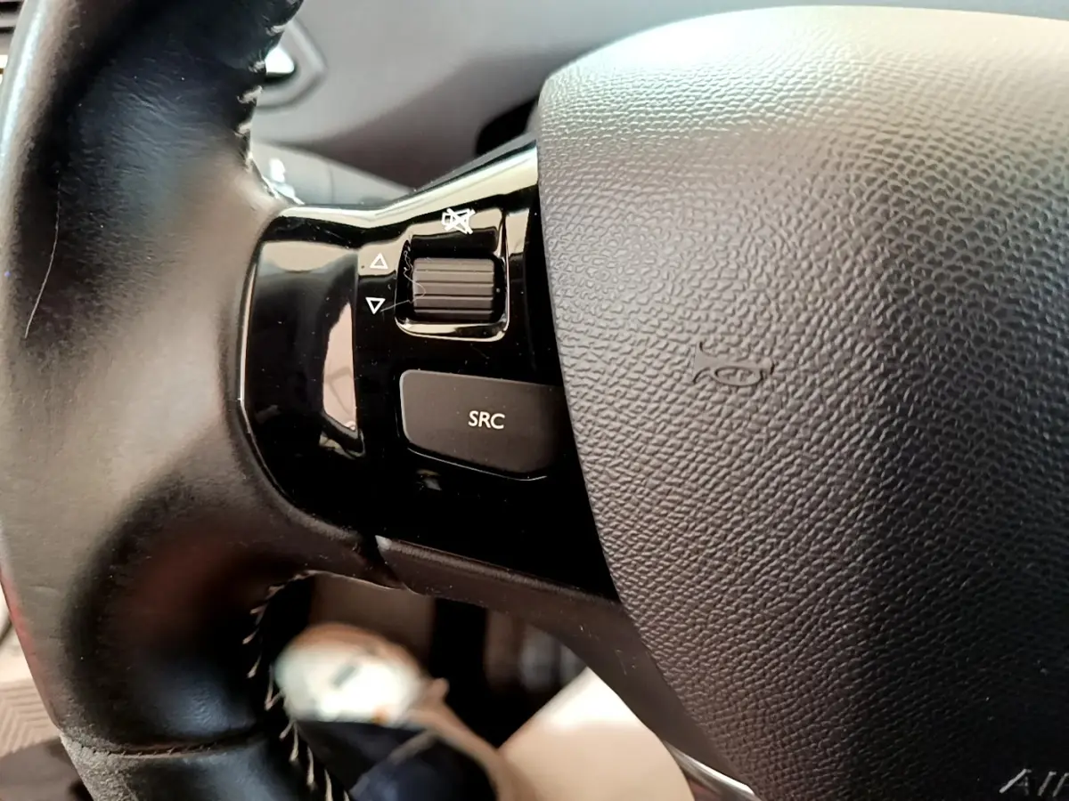 Gros plan sur le volant cuir noir de la Peugeot 308 avec commandes audio intégrées côté gauche.