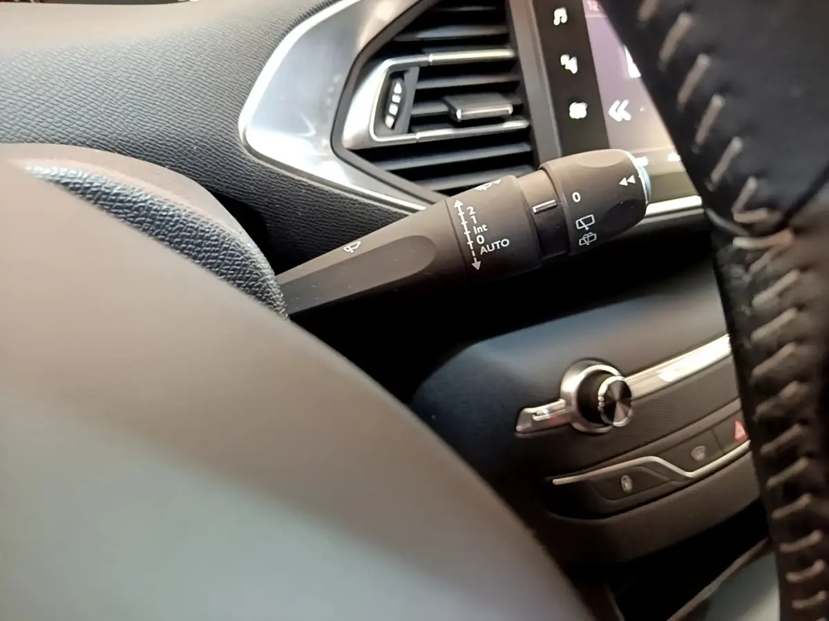 Gros plan sur la manette d'essuie-glace côté gauche du tableau de bord noir d'une Peugeot 308 blanche de 2017.