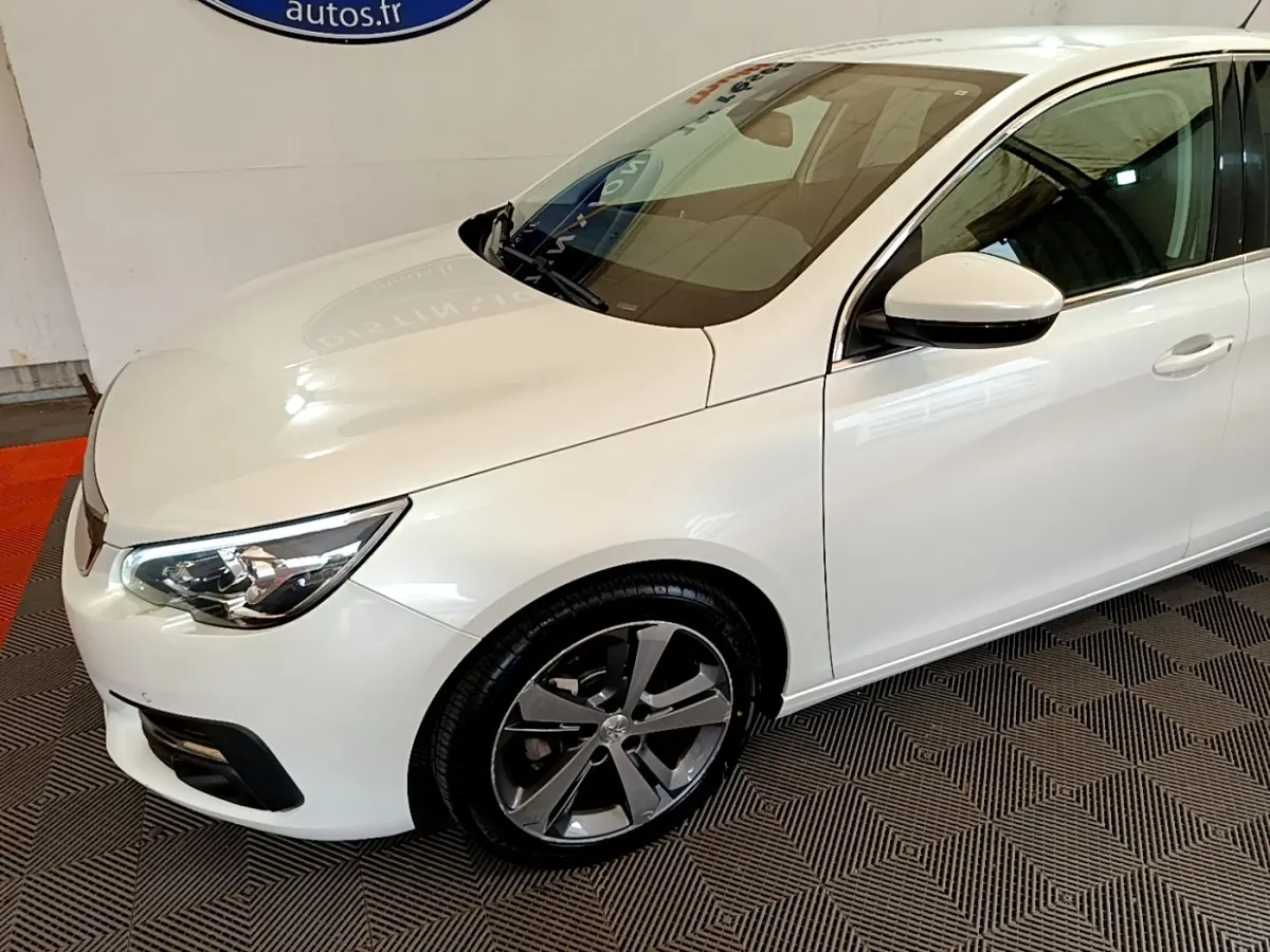 Vue 3/4 avant droit d'une Peugeot 308 blanche avec jantes alliage et phares LED ellipsoïdaux visibles.