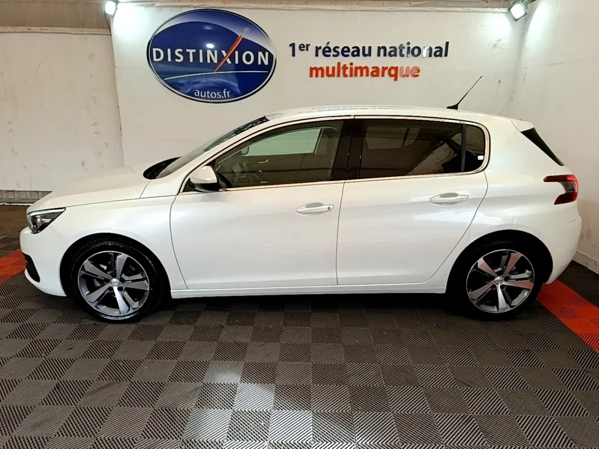 Profil côté gauche d'une Peugeot 308 blanche 2017, avec jantes alliage et vitres teintées, en intérieur showroom.