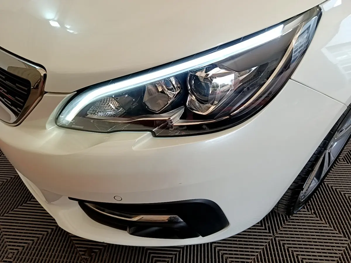 Gros plan sur le phare avant droit blanc d'une Peugeot 308 2017 avec feux LED et calandre partielle visible.