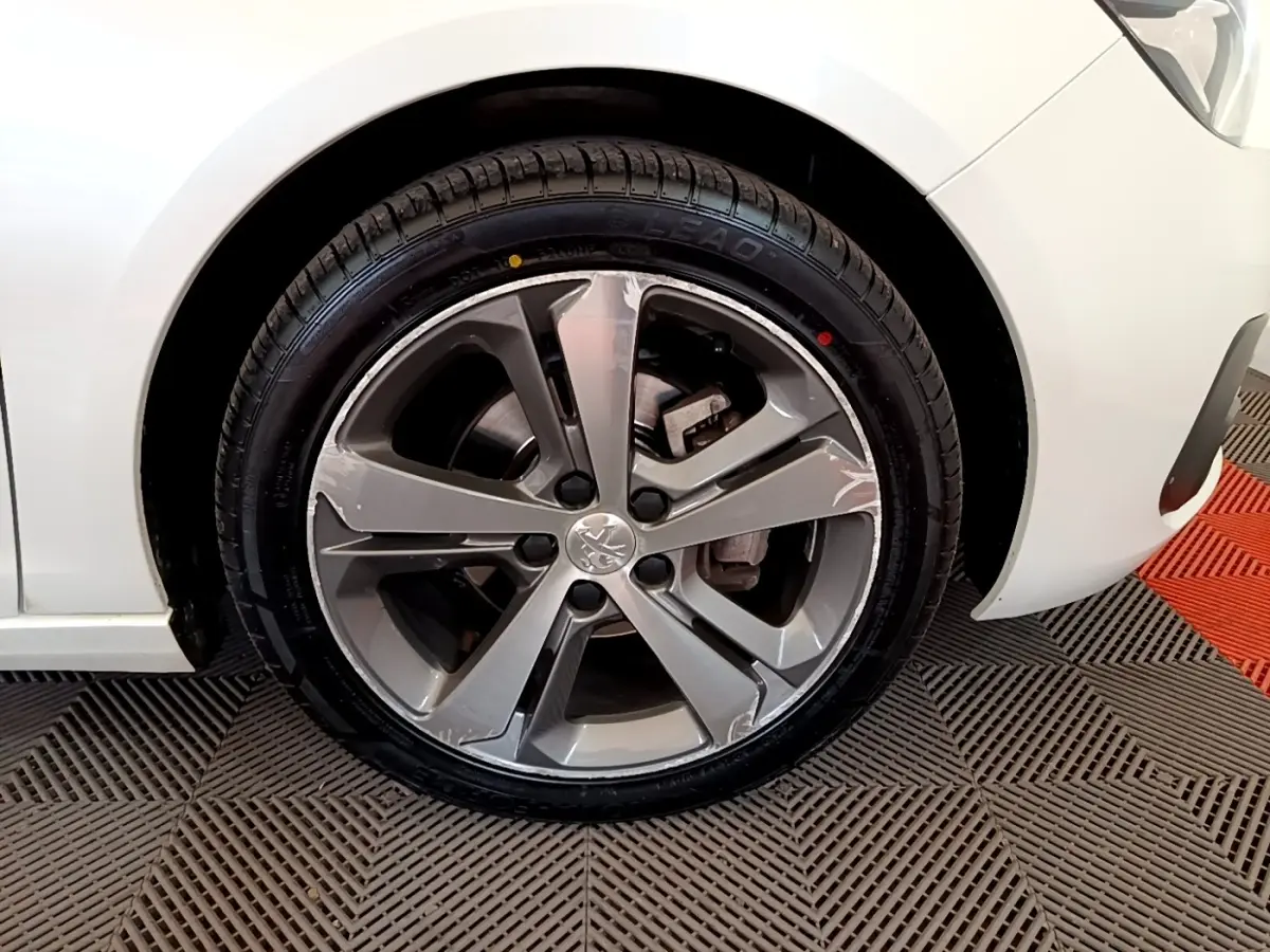 Gros plan sur la roue avant droite d'une Peugeot 308 blanche, mettant en valeur la jante alliage gris et le pneu neuf.