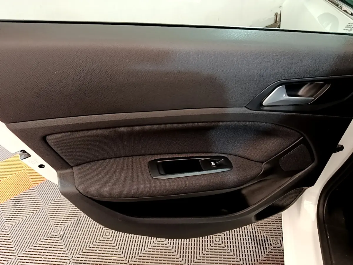 Vue intérieure de la porte côté gauche d'une Peugeot 308 blanche, avec habillage tissu noir et commande de vitre électrique.