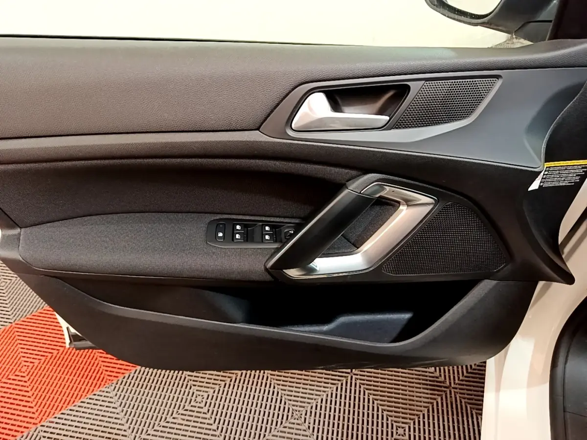 Vue rapprochée de la porte avant gauche noire de la Peugeot 308 blanche, avec poignée argentée et commandes de vitres.